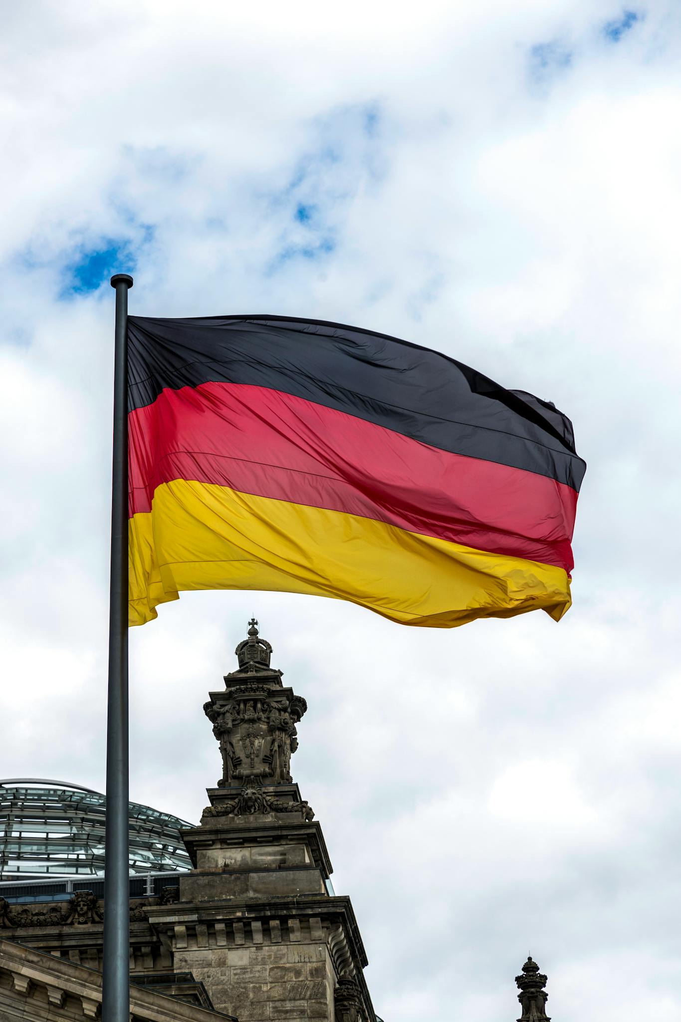 German flag fluttering above the Reichstag building in Berlin with a cloudy sky backdrop.